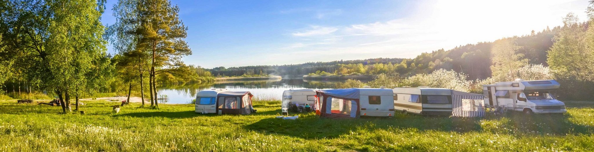 Das Bild zeigt Wohnwagen und Camper in einer idyllischen Seenlandschaft