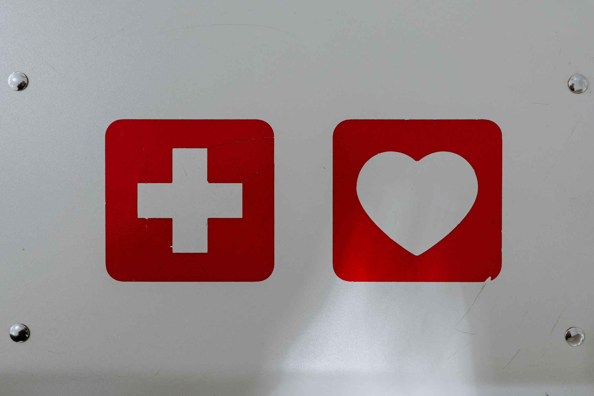 Piktogramme: Kreuz und Herz Das Bild zeigt Piktogramme eines roten Kreuzes und eines roten Herzens auf einer weißen Wand